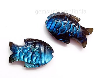 Puede incluir: Dos colgantes de pescado tallados en labradorita, uno azul y otro negro con reflejos azules iridiscentes.