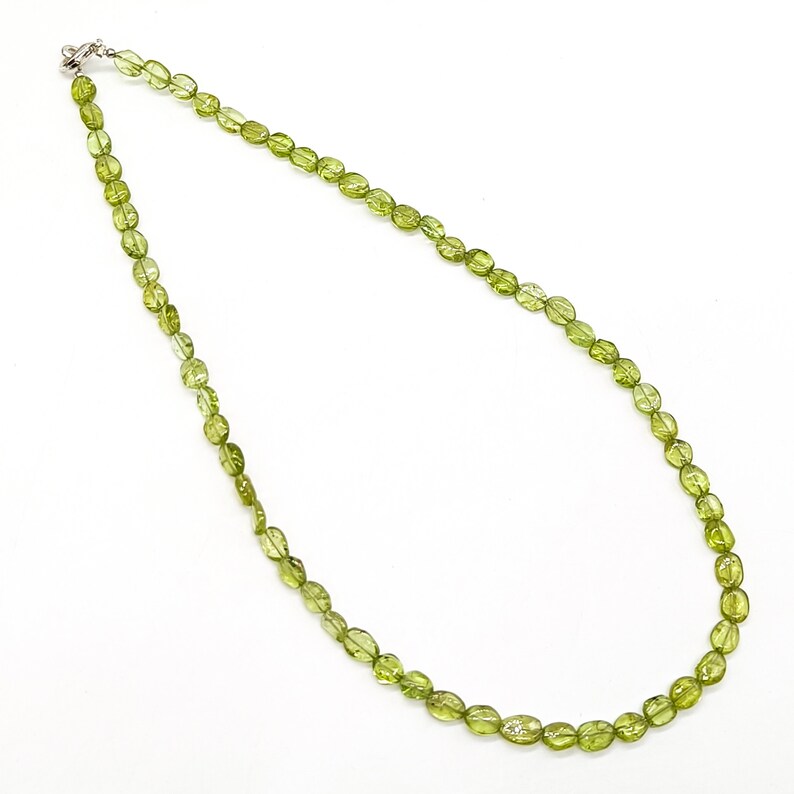May include: A green peridot gemstone necklace with oval-shaped beads. The necklace is made with a silver clasp.