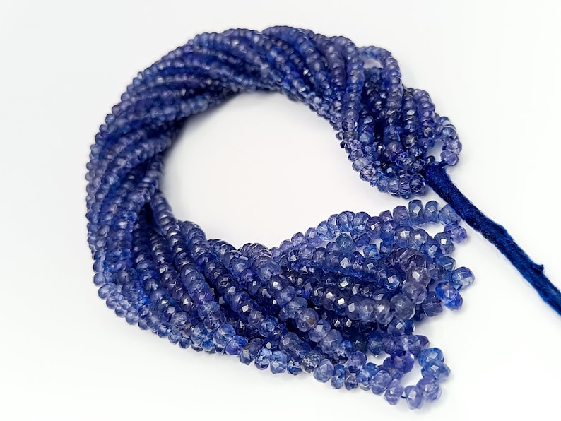 K&ouml;nnte beinhalten: Eine Str&auml;hne blauer Edelsteinperlen, wahrscheinlich Amethyst oder Saphir, mit facettenreicher, unregelm&auml;&szlig;iger Form. Die Perlen sind auf einer d&uuml;nnen Schnur aufgef&auml;delt und bereit f&uuml;r die Schmuckherstellung.