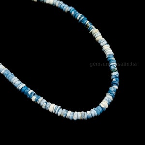 May include: A strand of blue and white opal beads, with a slightly irregular shape, strung together on a black background.