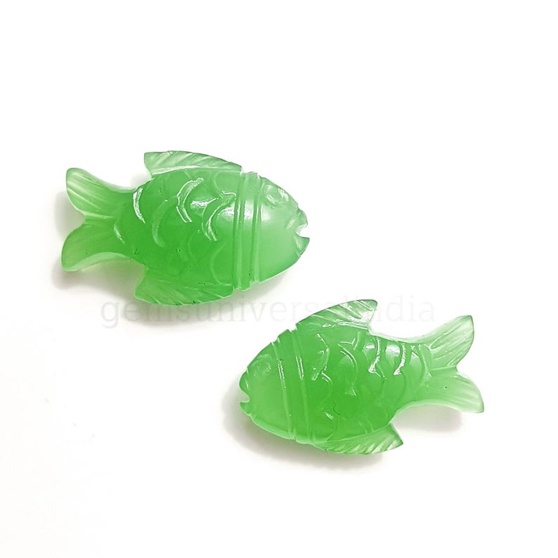 K&ouml;nnte beinhalten: Zwei gr&uuml;ne Jade-Fisch-Anh&auml;nger mit detaillierten Schnitzereien. Die Fische sind in entgegengesetzte Richtungen gerichtet und haben eine glatte, polierte Oberfl&auml;che.