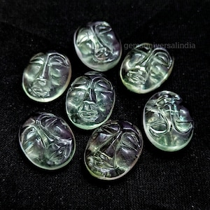 May include: Seven green face carvings made from fluorite. The carvings are oval shaped and have a translucent appearance.