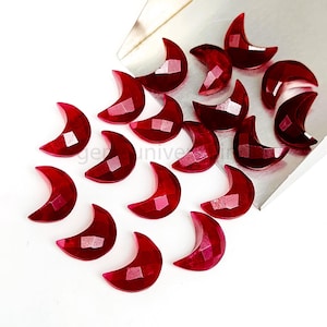 May include: A group of red crescent-shaped glass rhinestones, some are spilling out of a silver container.