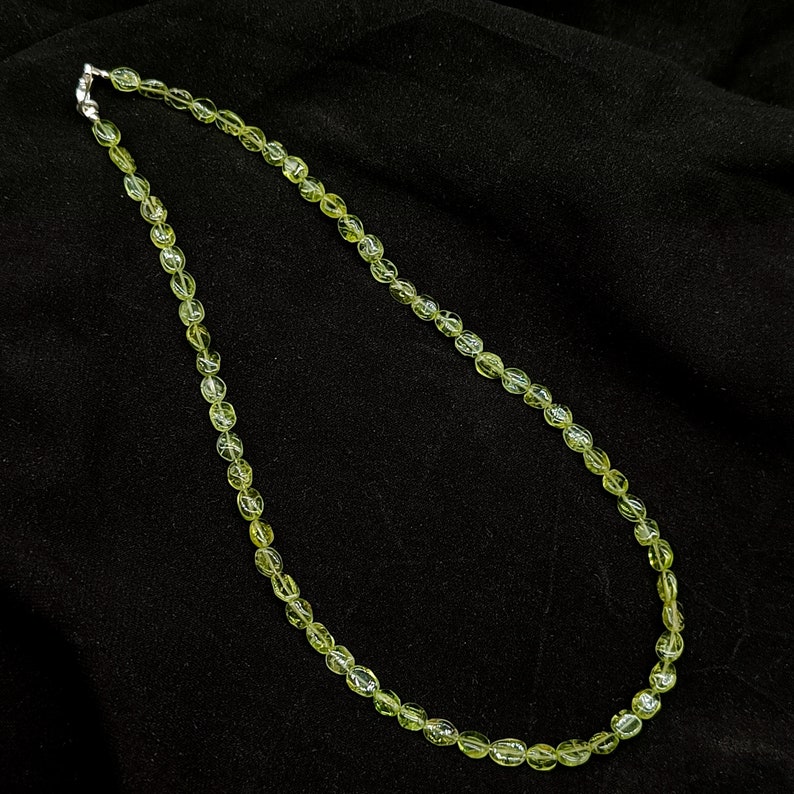 May include: A green gemstone necklace with oval-shaped beads. The necklace is made of natural stones and has a silver clasp.