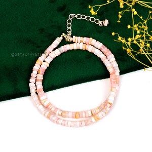 May include: A double strand necklace made of pink opal beads. The beads are small and round, and they are strung on a silver chain. The necklace is on a white background.