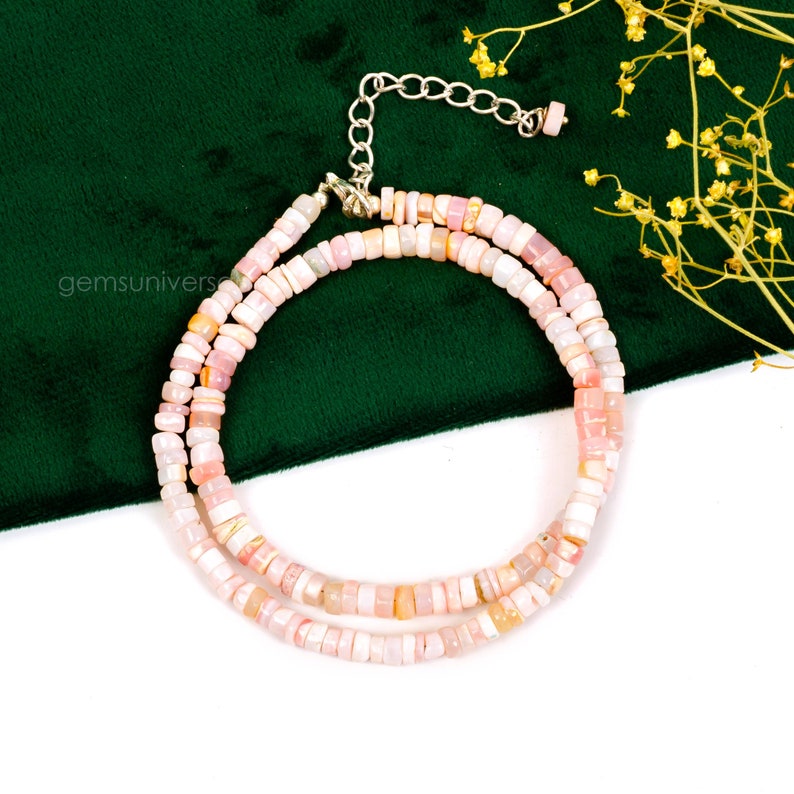 May include: A double strand necklace made of pink opal beads. The beads are small and round, and they are strung on a silver chain. The necklace is on a white background.