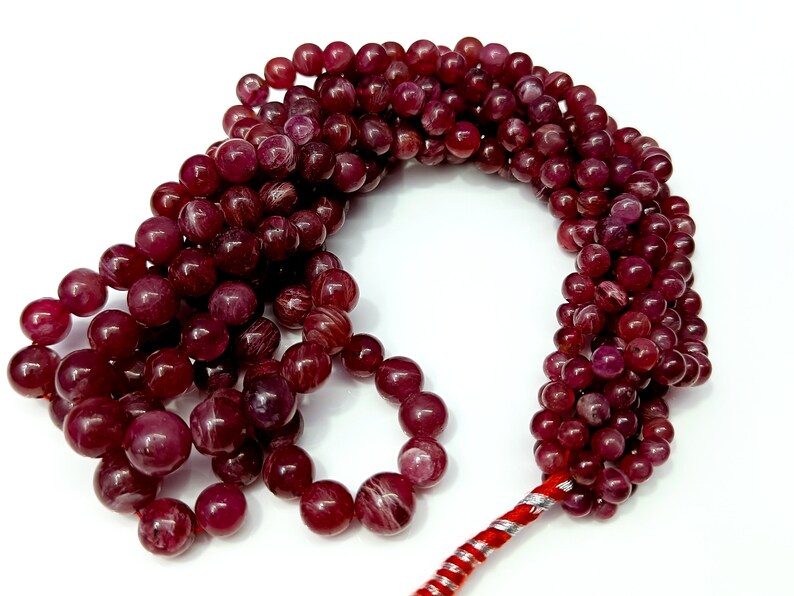 May include: A strand of deep red gemstone beads with a red and silver cord. The beads are round and have a smooth, polished finish.