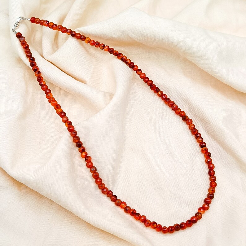Puede incluir: Un collar largo hecho de peque&ntilde;as cuentas redondas de cornalina de color naranja rojizo.