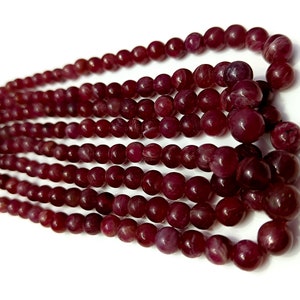 May include: A strand of deep red gemstone beads. The beads are round and have a smooth, polished finish.