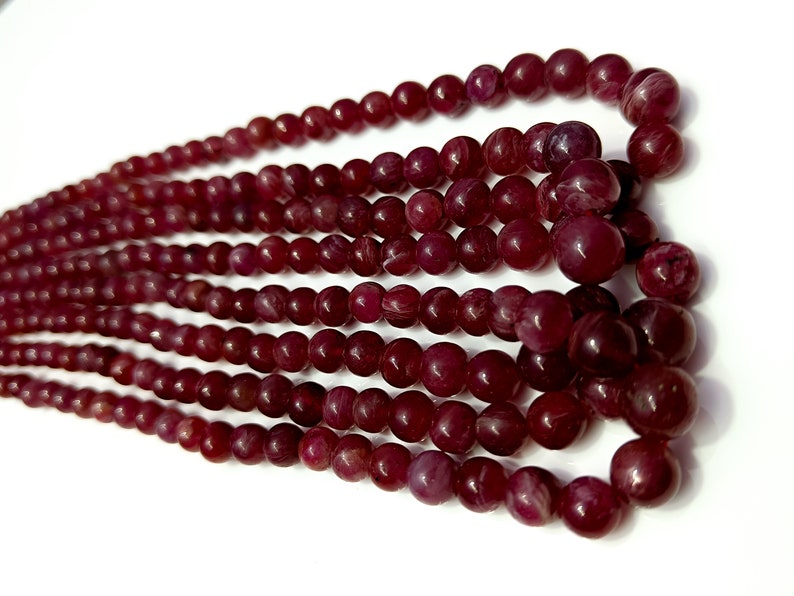 May include: A strand of deep red gemstone beads. The beads are round and have a smooth, polished finish.