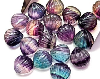 May include: A collection of 17 heart-shaped fluorite gemstones, each carved with a shell design. The gemstones are a mix of purple, blue, and green hues.