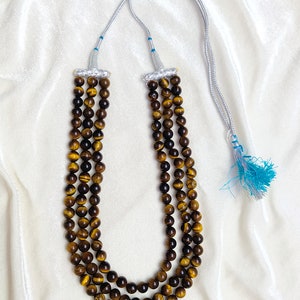 May include: A three-strand necklace made of brown tiger's eye beads with a silver cord and a blue tassel.