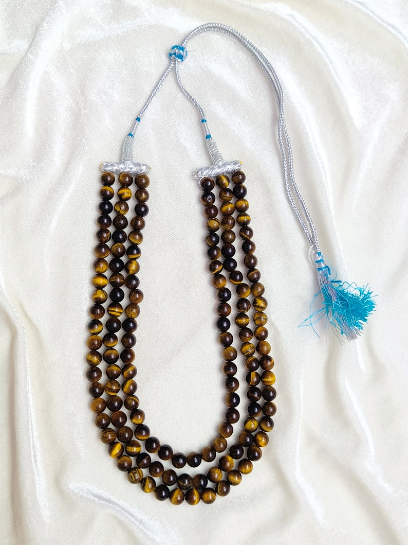 May include: A three-strand necklace made of brown tiger's eye beads with a silver cord and a blue tassel.