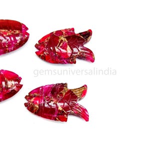 May include: Four red gemstone fish carvings with gold flecks. The fish are carved in a detailed, realistic style.