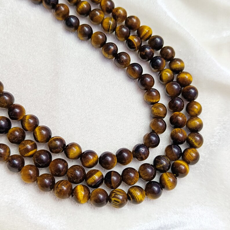 May include: A strand of tiger's eye beads in shades of brown and gold. The beads are round and smooth, and they are strung on a clear cord.