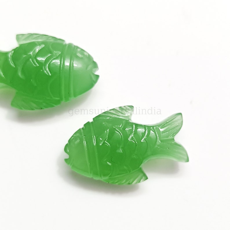 K&ouml;nnte beinhalten: Zwei gr&uuml;ne Jade-Fisch-Anh&auml;nger mit detaillierten Schnitzereien. Die Fische sind in verschiedene Richtungen ausgerichtet und haben eine glatte, polierte Oberfl&auml;che.