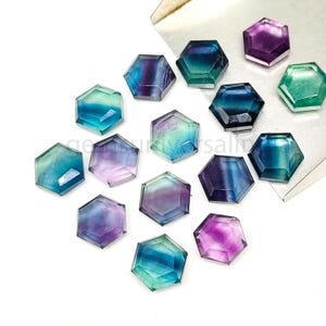 May include: Assortment of 13 hexagonal fluorite gemstones in various shades of green, blue, and purple. The gemstones are faceted and have a smooth, polished finish.