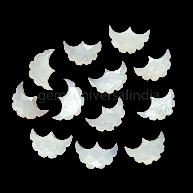 May include: A collection of 13 white mother of pearl crescent moon shaped cabochons. The cabochons are faceted and have a pearlescent sheen.