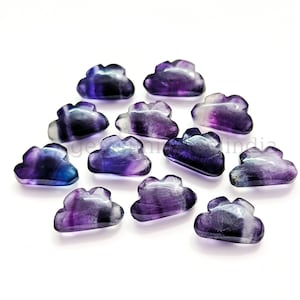 May include: A collection of twelve purple and blue fluorite cloud shaped cabochons. The cabochons are polished and have a smooth, glossy finish.