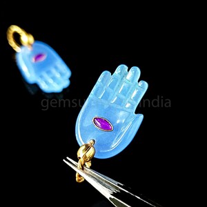 May include: Two blue glass hand charms with gold accents and a pink gemstone in the center. The charms are hanging from gold chains.