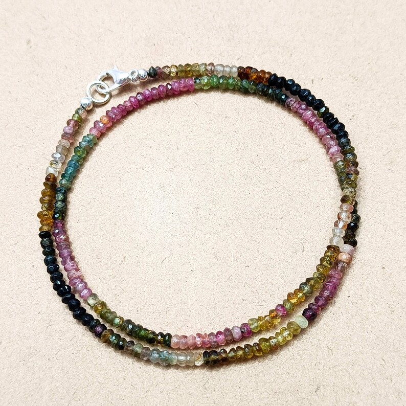May include: A multi-colored gemstone necklace with a silver clasp. The necklace is made of small, round beads in shades of pink, green, black, and brown.