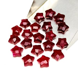 Può includere: Una collezione di 20 pietre preziose rosse a forma di stella. Le pietre preziose sono sfaccettate e hanno una finitura lucida.