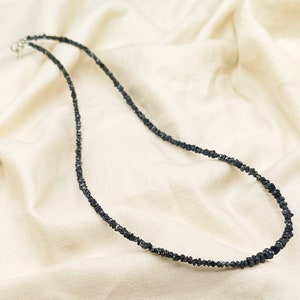 May include: A black diamond necklace made of small, rough-cut diamonds strung together on a silver chain.