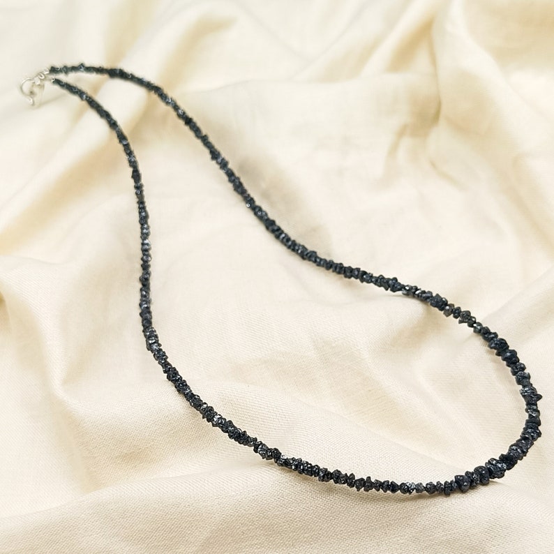 May include: A black diamond necklace made of small, rough-cut diamonds strung together on a silver chain.