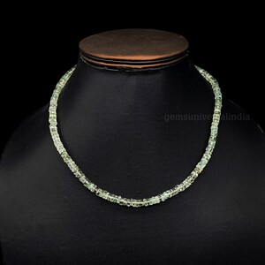 May include: A light green gemstone necklace made of small, square-shaped beads. The necklace is displayed on a black mannequin bust.