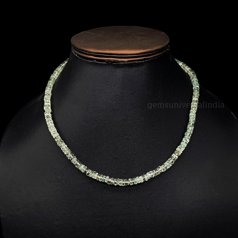 May include: A light green gemstone necklace made of small, square-shaped beads. The necklace is displayed on a black mannequin bust.