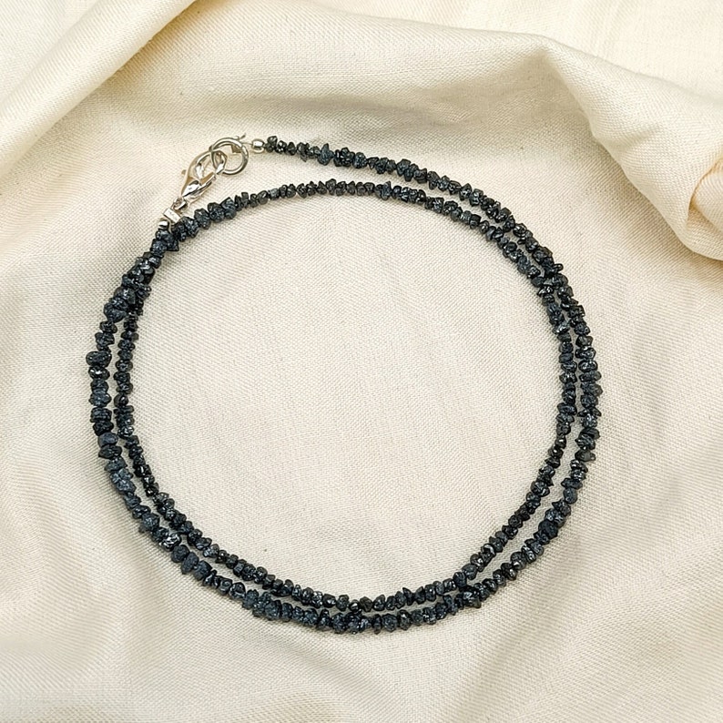 May include: A black diamond necklace with a silver clasp. The necklace is made of small, rough-cut black diamonds.