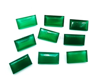 May include: Ten green rectangular gemstones, likely emeralds, are arranged on a white surface. The gemstones are smooth and polished, with a slight sheen.