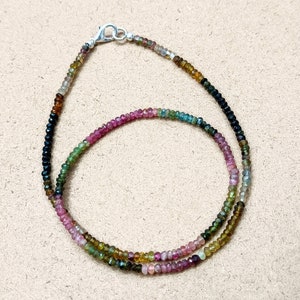 May include: A multi-colored gemstone necklace with black, green, pink, and yellow beads. The necklace is made of small, round beads and has a silver clasp.