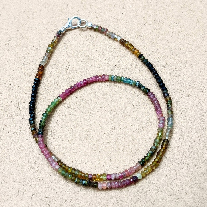 May include: A multi-colored gemstone necklace with black, green, pink, and yellow beads. The necklace is made of small, round beads and has a silver clasp.