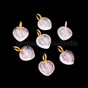 May include: Seven pink heart-shaped gemstone pendants with gold-coloured jump rings. The pendants are translucent and have a slight shimmer.