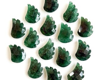 Puede incluir: Una colección de colgantes de piedras preciosas verdes, cada uno con un diseño único, texturizado, en forma de ala. Las piedras preciosas están facetadas, captando la luz y mostrando una gama de tonos verdes oscuros y claros. Los colgantes están dispuestos sobre un fondo blanco.