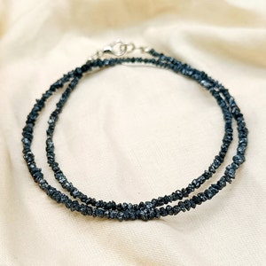 May include: A double strand necklace made of black rough diamonds. The necklace is made of small, irregular shaped diamonds that are strung together on a silver chain.
