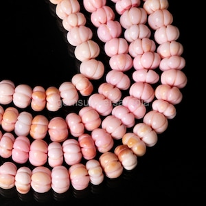 May include: Close-up of strands of pink gemstone beads. The beads are carved into a pumpkin shape, with a light pink colour and a glossy finish. The beads are strung together, creating a necklace or bracelet.