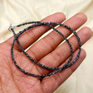 May include: A black diamond necklace made of small, rough-cut black diamonds. The necklace is approximately 18 inches long and is strung on a silver chain.