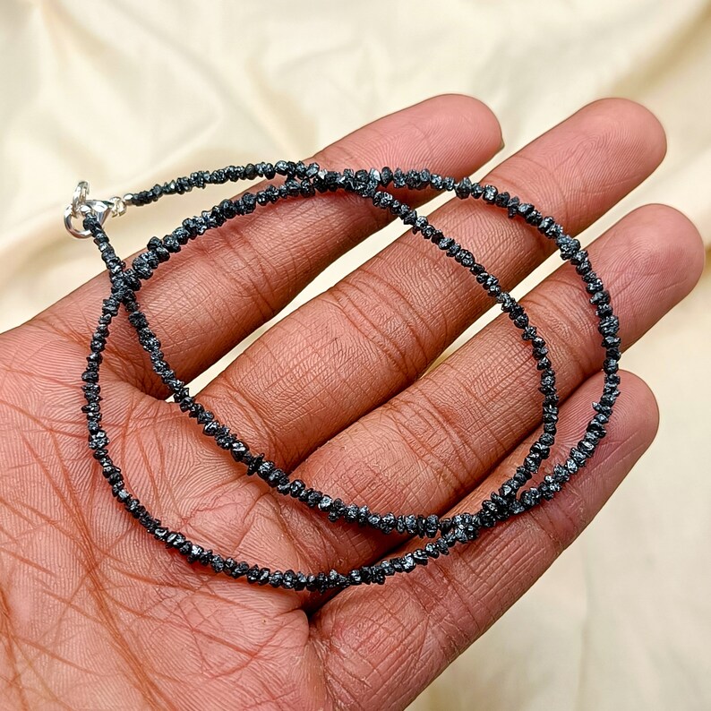 May include: A black diamond necklace made of small, rough-cut black diamonds. The necklace is approximately 18 inches long and is strung on a silver chain.