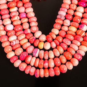 Puede incluir: Una hebra de cuentas de coral rosa y naranja. Las cuentas son de forma ovalada y tienen un acabado liso y pulido.