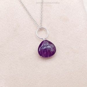 May include: A silver chain necklace with a purple amethyst pendant shaped like a seashell. The pendant is carved with lines to resemble the ridges of a seashell.