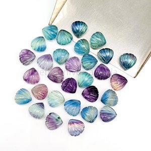 May include: A collection of 20 carved gemstone cabochons in various shades of blue, purple, and green. The cabochons are shaped like seashells and have a smooth, polished finish.