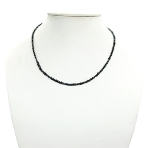 May include: A black diamond necklace with small, irregular shaped stones. The necklace is on a white mannequin bust.