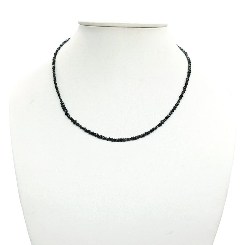 May include: A black diamond necklace with small, irregular shaped stones. The necklace is on a white mannequin bust.