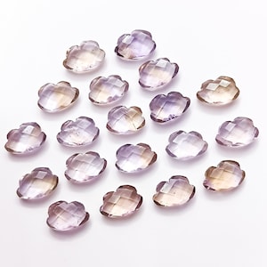 May include: A collection of 18 amethyst and citrine gemstone flower-shaped cabochons. The stones are a mix of light purple and yellow.