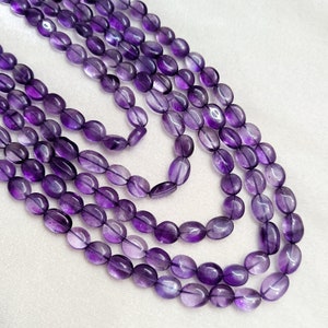 May include: Several strands of amethyst gemstone beads. The beads are oval-shaped and range in color from light to deep purple. The strands are arranged in a layered pattern, showcasing the natural variations in color and translucence of the stones.