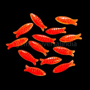 Può includere: Un gruppo di 12 caramelle gommose a forma di pesce arancioni su uno sfondo nero.