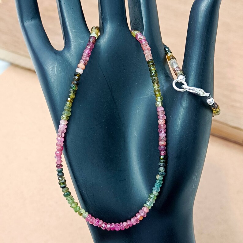 May include: A multi-colored gemstone necklace with pink, green, and black beads. The necklace is made with a silver clasp.