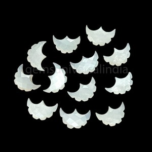 May include: A collection of 12 white mother of pearl crescent moon shaped cabochons. The cabochons are approximately 1 inch in length and have a slightly iridescent finish.